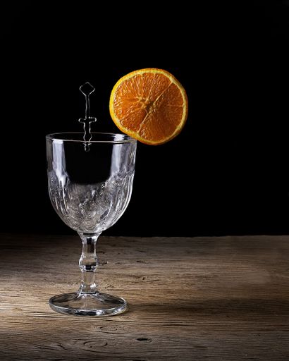 A vertical shot of a glass with an orange slice on a wooden table with dark background