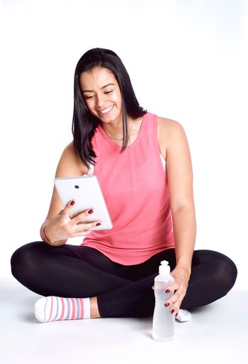 A vertical shot of a Hispanic female using her tablet sitting isolated on a white background