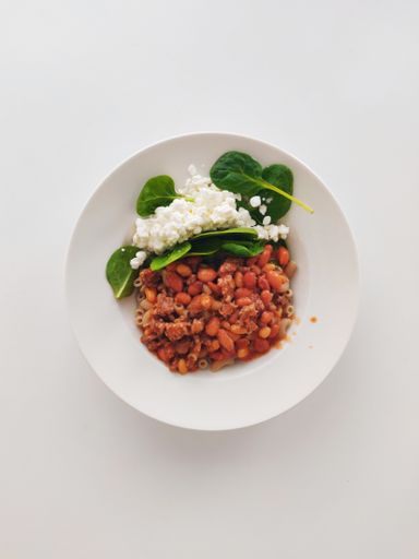 A vertical shot of stewed beans with cheese and greens in a white plate