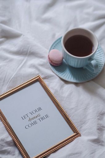 A cup of coffee and pastries on a bed, with a framed photo on the sheets
