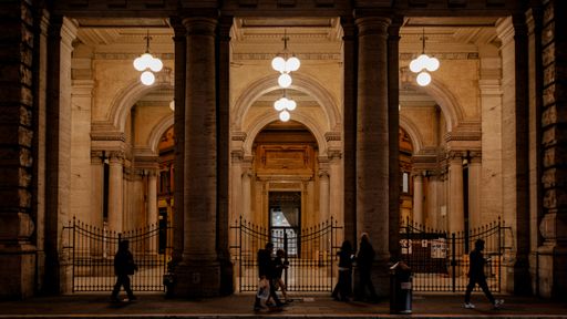 A crowd strolling at night near a grand building, illuminated by lights in Rome, Italy