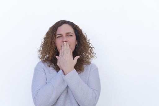 attractive blonde woman with curly hair and blue eyes covering her mouth with her hands looking at the camera with white background and copy space