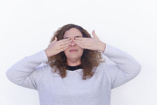 beautiful blonde curly-haired woman dressed in white, covering her eyes with her hands on a white background and copyspace