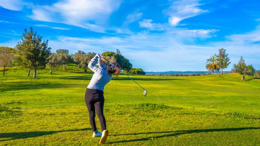 A female golfer hitting a tee shot on a sunny day at a golf course