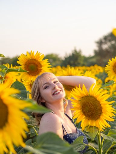 A portrait of a joyful blonde woman relaxing in the sunflower field on a sunny day