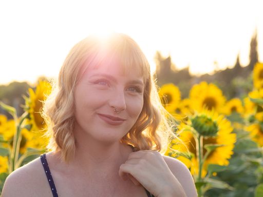 A portrait of a cheerful young lady in the sunlight; a sunflower field in the background