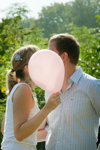 A vertical shot of a couple kissing behind a pink balloon in the nature