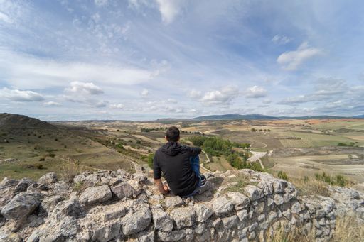 Thoughtful person in sportswear sitting on a rock on top of a lookout point enjoying the wide views of the plains of castilla la mancha.