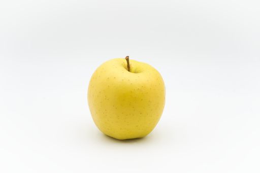A yellow apple on a white surface