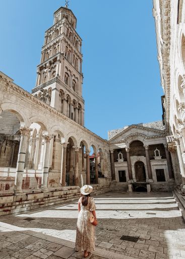 Rear view of young woman wearing stylish long dress standing in amazing square inside ancient Diocletian palace in Split in Croatia.