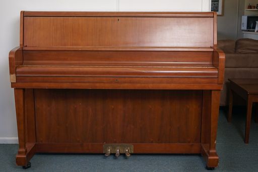 A brown piano against a white wall under the lights in a house
