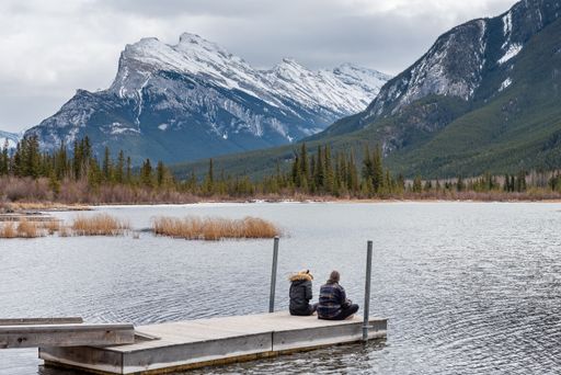 Two girls or women sitting on the dock at Vermilion Lakes in Banff National Park with Mount Rundle in the background