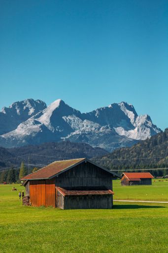 A view of small farm houses in an open green field with high rocky mountains in the background