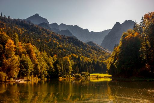A horizontal sunset wallpaper - lush green forest trees reflected on a tranquil lake under a clear sky