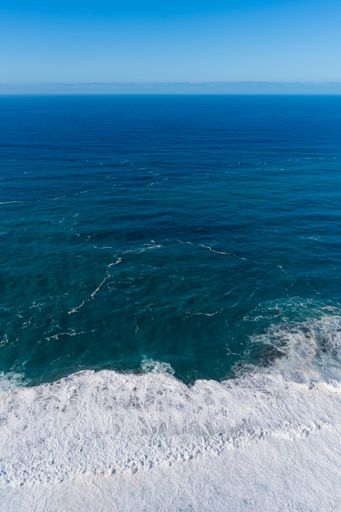 A vertical shot of the North Atlantic ocean with gentle white tides at the shore under a clear sky on a sunny day