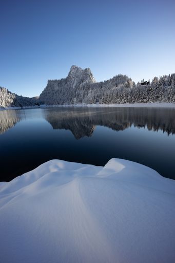 Winter morning landscape view of an illuminated mountain range reflecting on the surface of a lake with a snow dune in the foreground