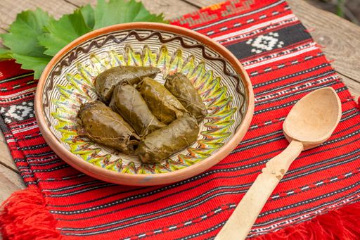 A close-up shot of shrub dolma in the wooden plate and a wooden spoon on red traditional carpet