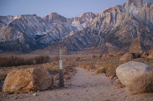 A trail marker signs a hiking path in Calfornia's Alabama Hills area with a picturesque background of the Sierra Nevada mountains.