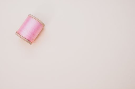 A pink sewing thread isolated on a light background with free space for text
