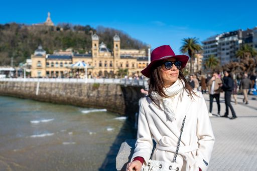 A woman in a white coat strolling on the sidewalk with a purse