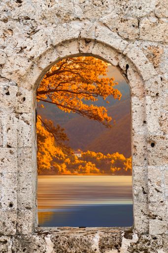 A vertical shot of autumn scenery through a stone arched window