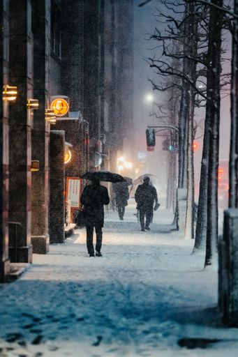 Pedestrians stroll along a snowy city sidewalk during a storm