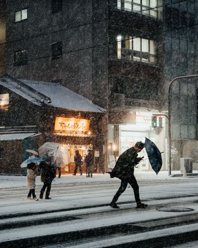 A man with an umbrella crossing a snowy urban street