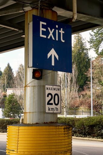 A blue and white exit sign and a posted speed limit sign of 20 km per hr.