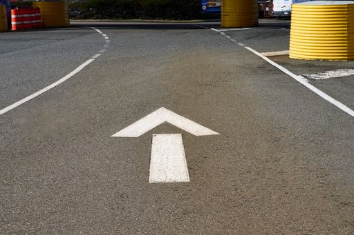 White arrow painted between two lines on the pavement at a ferry terminal indicating the direction of travel is straight.