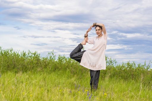 Young woman performs yoga exercises. Stands on a green field against the blue summer sky. Healthy lifestyle.