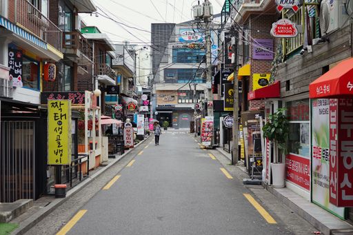 Side street with restaurants and taverns, older woman walking with a parasol, visible power supply/network cables. Seoul, South Korea, 30th June 2019.