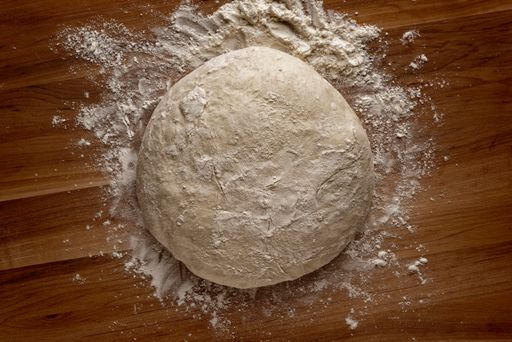 A top view of a ball of bread dough on a wooden board with flour