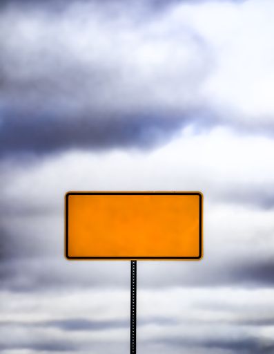 A yellow directional sign against cloudy sky