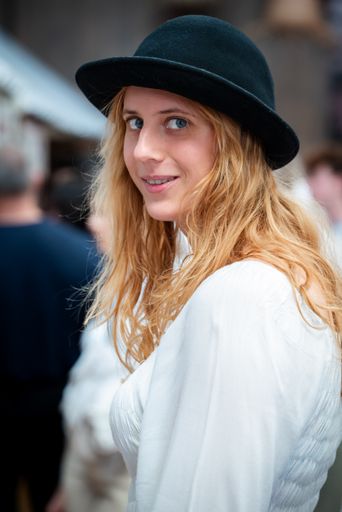 A blonde girl in a bowler hat and white shirt looking back at the camera