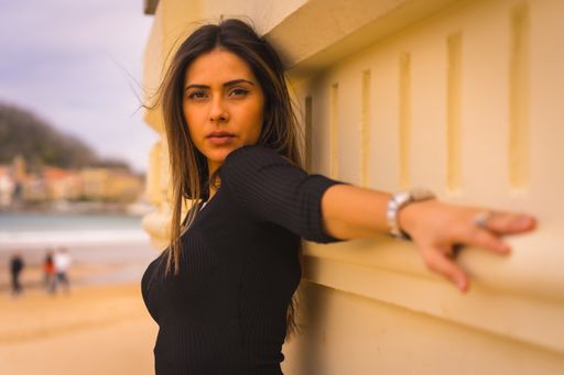 A pretty young Caucasian brunette in a short black dress, summer vacation, looking at camera with seductive gaze on the beach by the sea