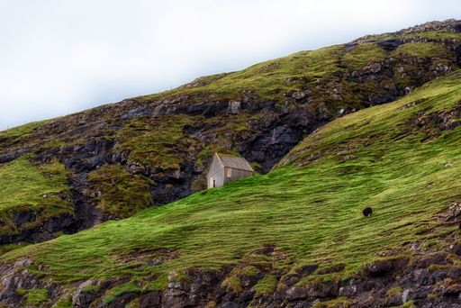 A scenic view of a wooden house on a green hill in the Faroe Islands