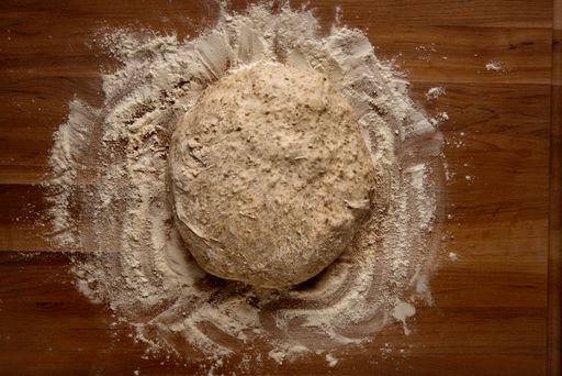 A top view of a ball of bread dough on a wooden board with flour
