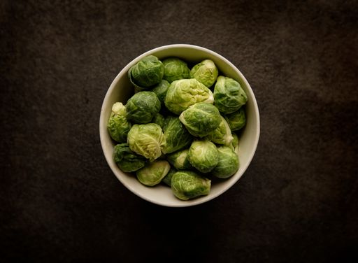 A top view of brussels sprouts in a white bowl on a wooden table
