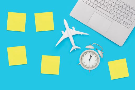 A top view of an airplane figurine, alarm clock, sticky notes and a computer- travel for business concept