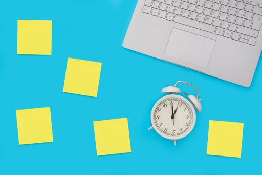 A top view of a blue background with sticky notes, an alarm clock, and a computer keyboard