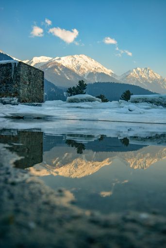 A vertical shot of a river reflecting the snowy hills on a winter day