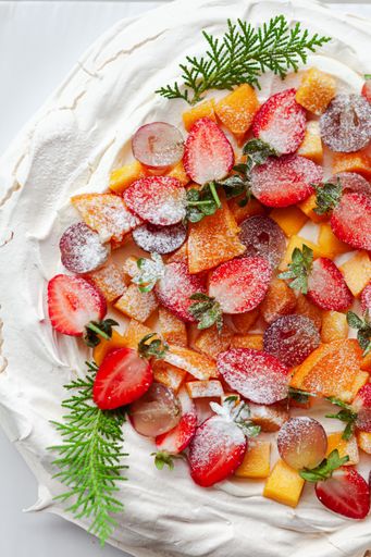 A white  pavlova cake adorned with fresh berries and a touch of greenery