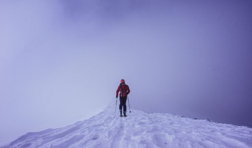 A man in red jacket strolling on snowy hilltop.