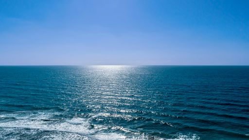 A scenic view of the sun shining over ocean waves reaching shore