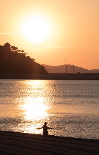A vertical shot of a silhouetted man welcoming the sunset at the Costa Brava beach, Catalonia