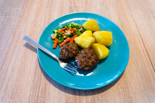 A closeup shot of boiled potatoes, grilled meat and vegetables in a blue plate