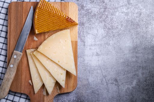 a top view of triangle pieces of cured Manchego cheese and a sharp knife on a wooden food board