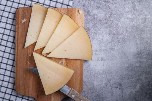a top view of triangle pieces of cured Manchego cheese and a sharp knife on a wooden food board