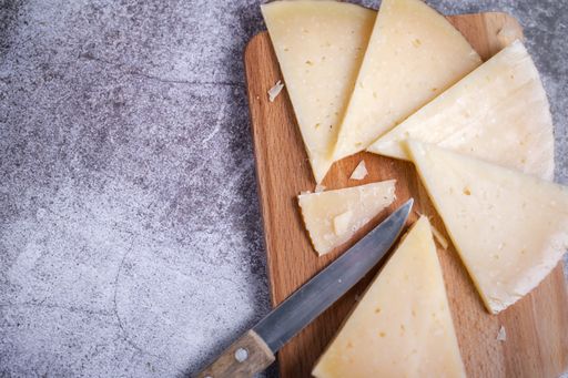 a top view of triangle pieces of cured Manchego cheese and a sharp knife on a wooden food board