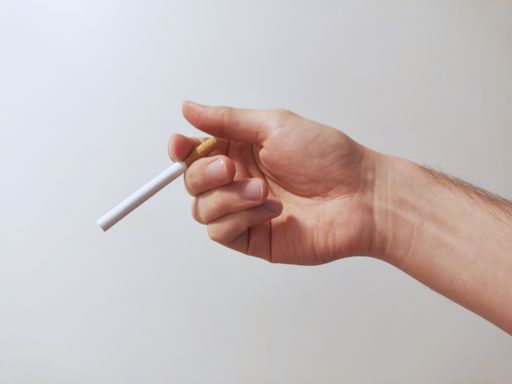A closeup shot of a person's hand holding a cigarette against a white background